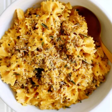 Creamy pumpkin pasta served in a bowl with herbs and cheese on top.
