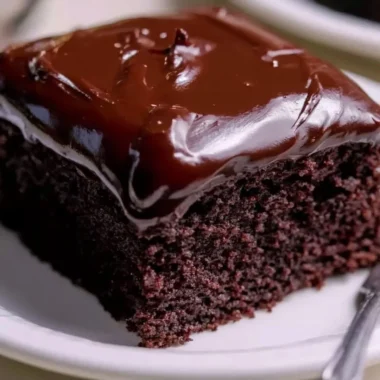 Wacky Chocolate Cake topped with sprinkles and chocolate drizzle on a rustic plate.