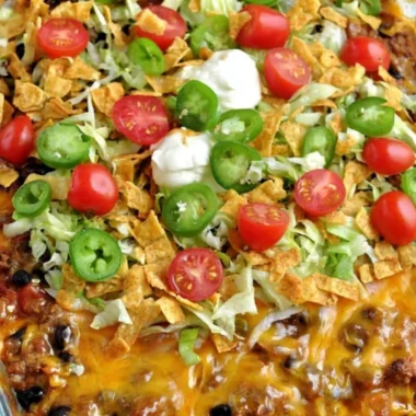 A delicious Walking Taco Casserole topped with cheese, lettuce, and tomatoes.