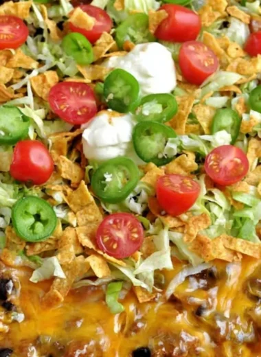 A delicious Walking Taco Casserole topped with cheese, lettuce, and tomatoes.
